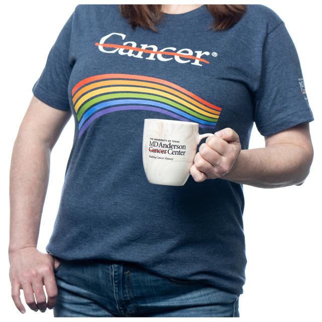 MD Anderson employee holding a marble ceramic mug with the black MD Anderson logo on it, also wearing a denim rainbow t-shirt featuring the white cancer strikethrough logo.